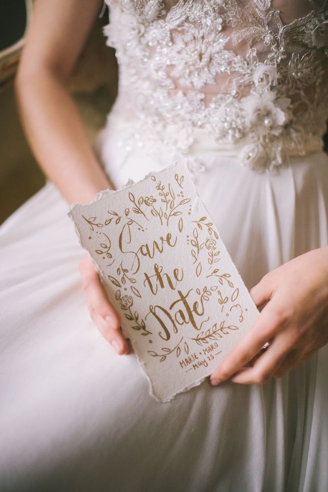 A woman in a white dress is holding a save the date card.