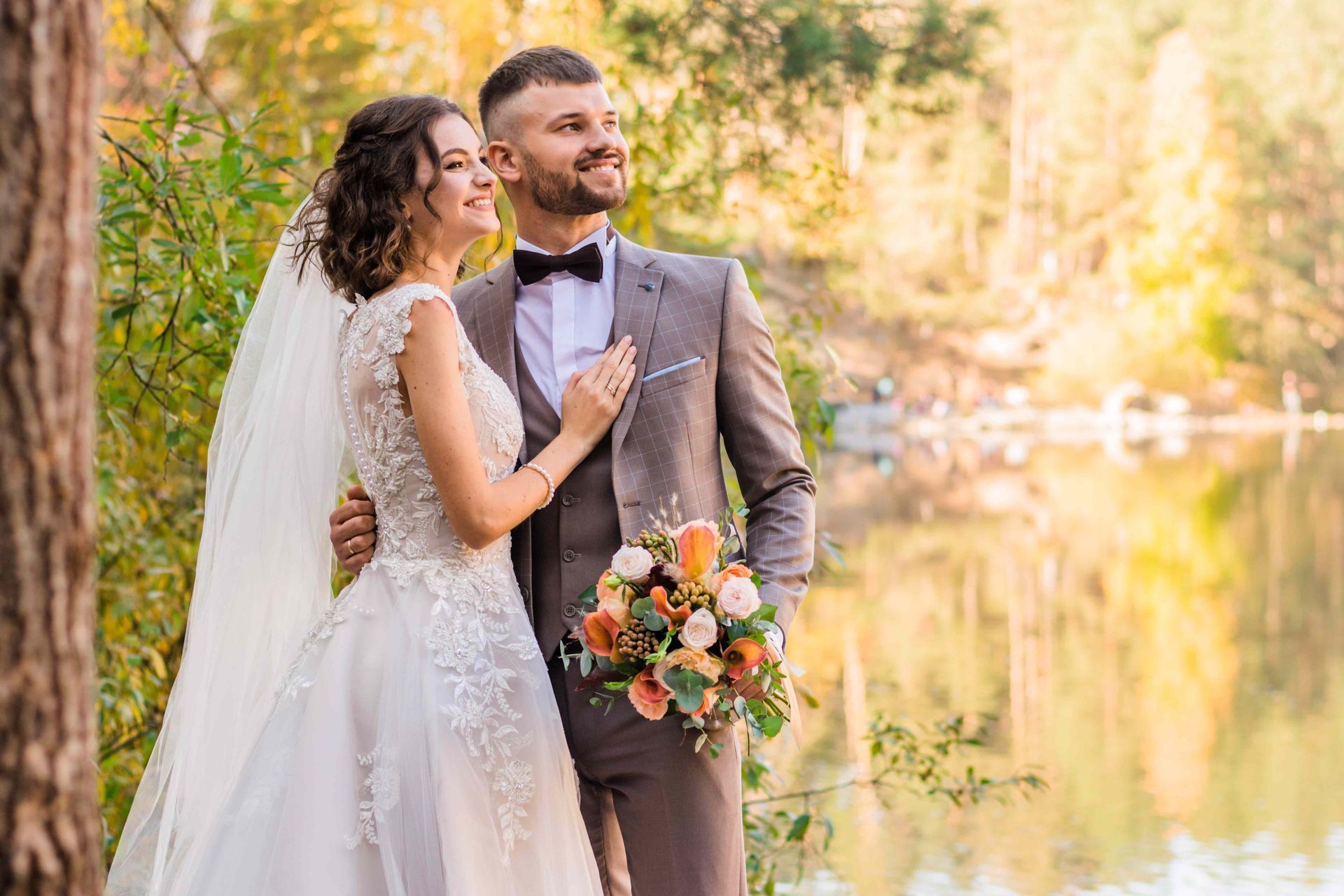 A bride and groom are posing for a picture in front of a lake.