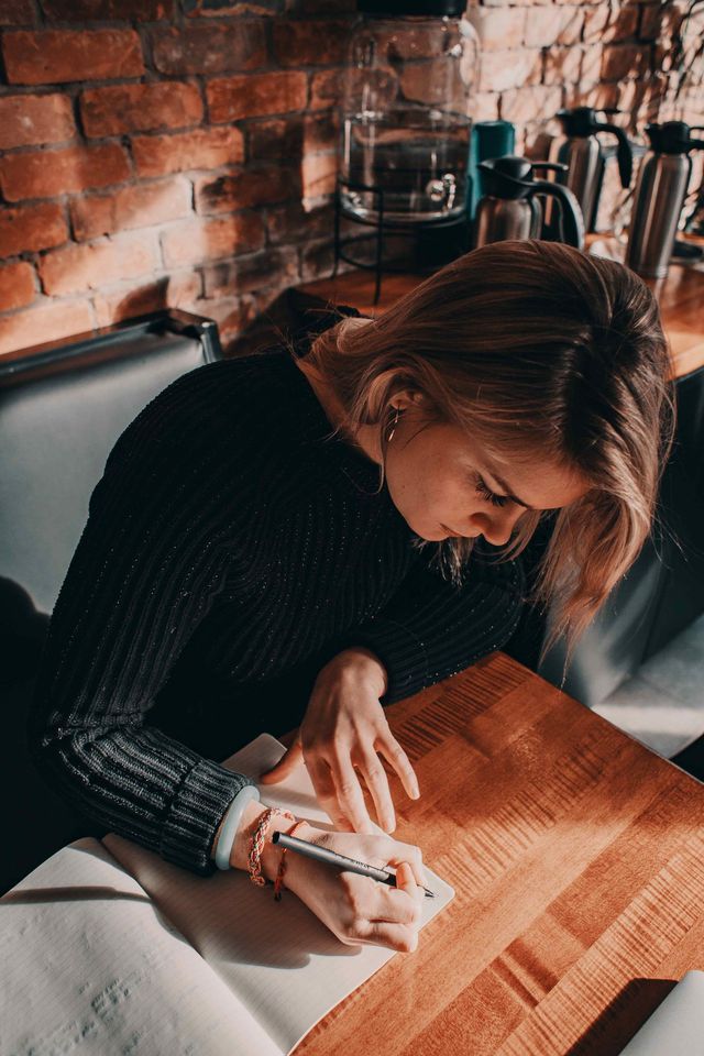 A woman is sitting at a table writing in a notebook.