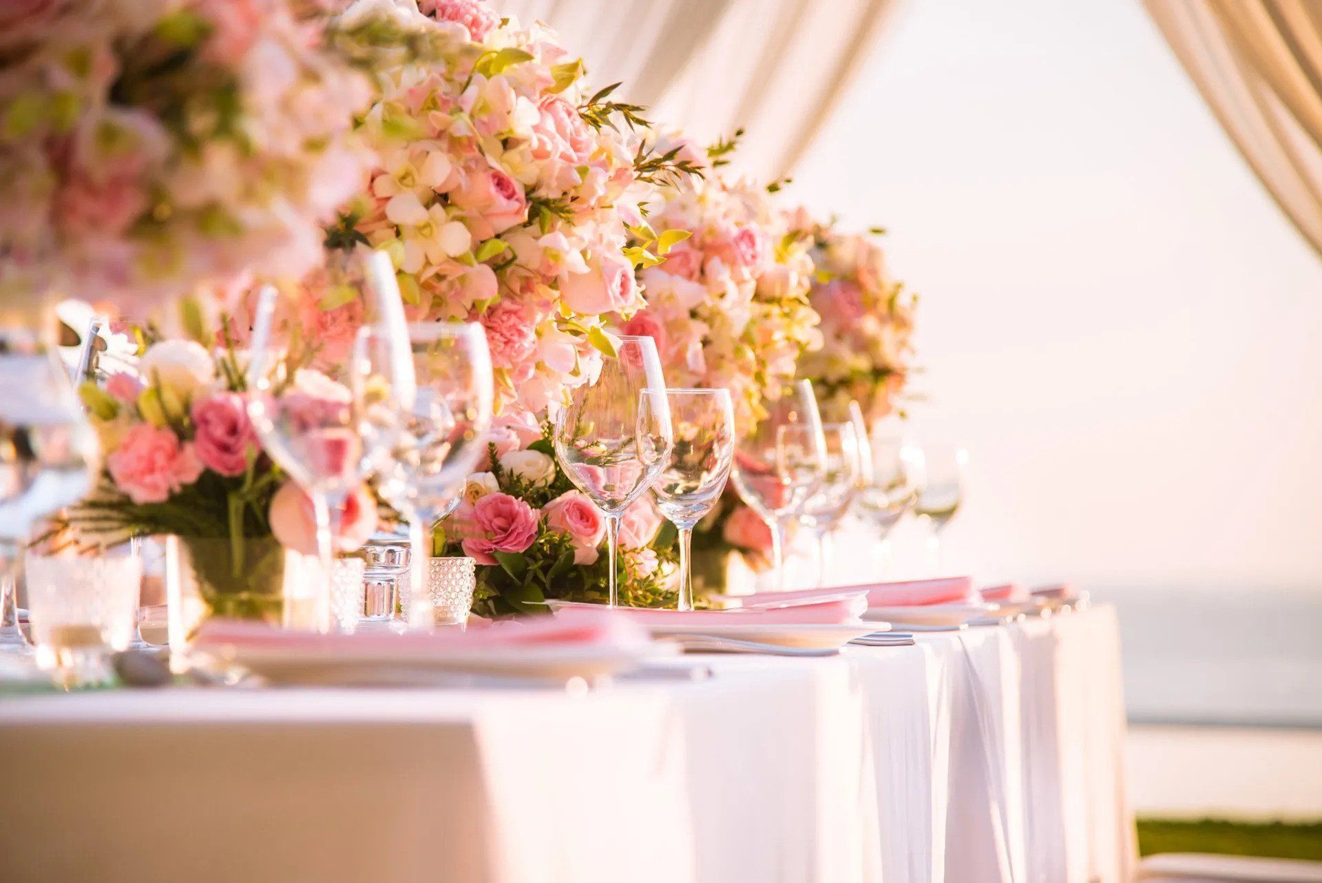 A long table set for a wedding reception with pink flowers and wine glasses.