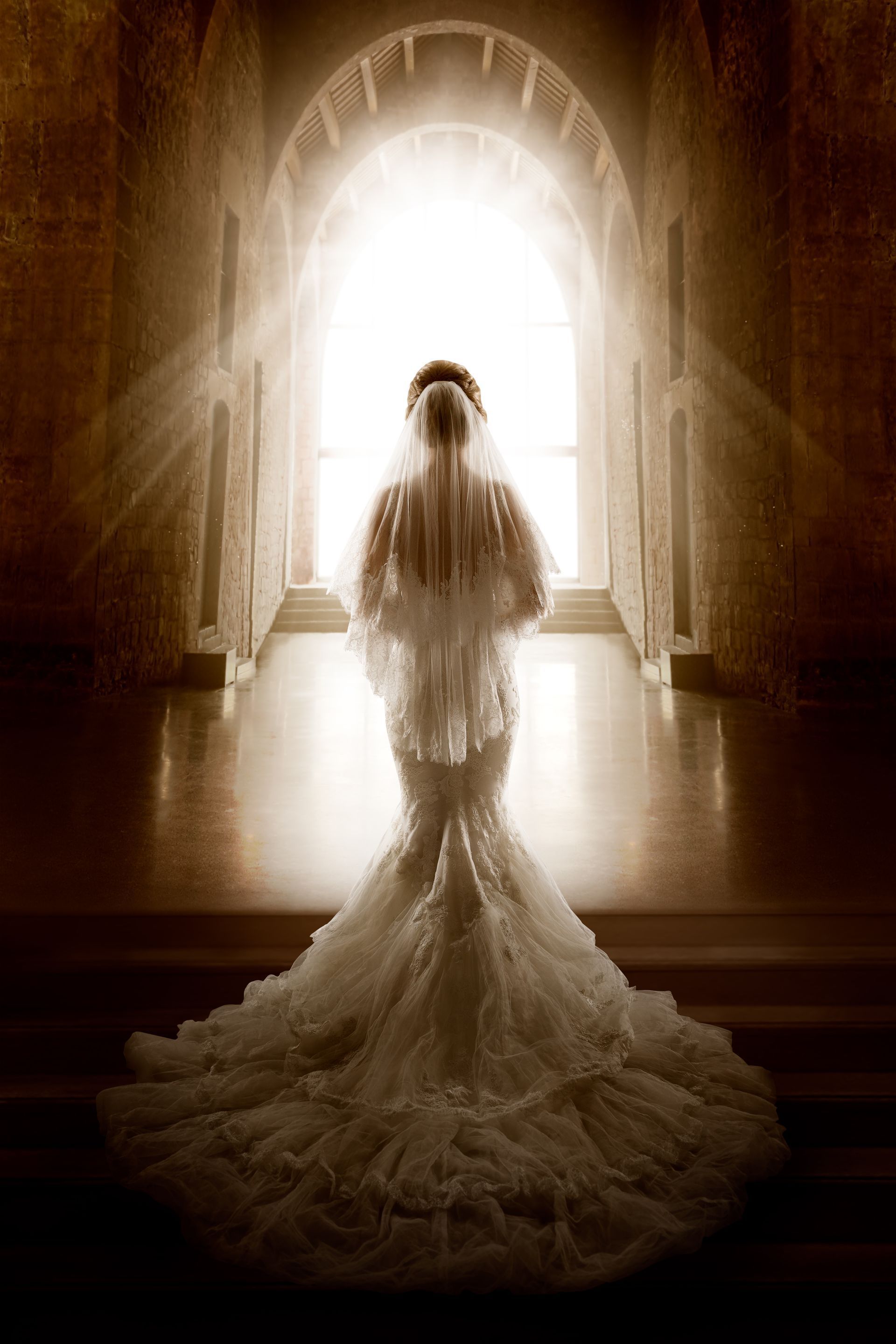 A bride in a wedding dress and veil is standing in front of a window.