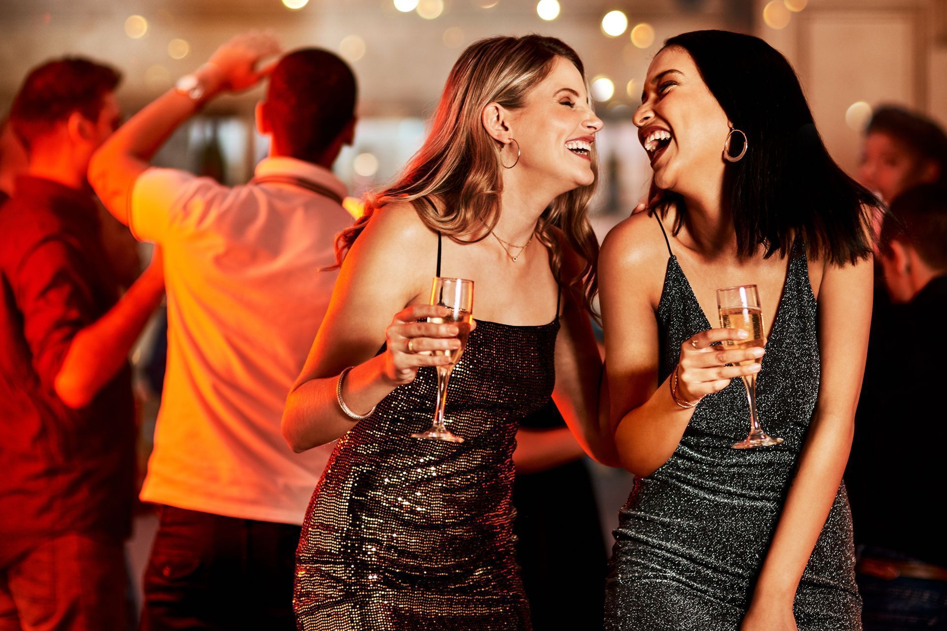 Two women are holding champagne glasses and laughing at a party.