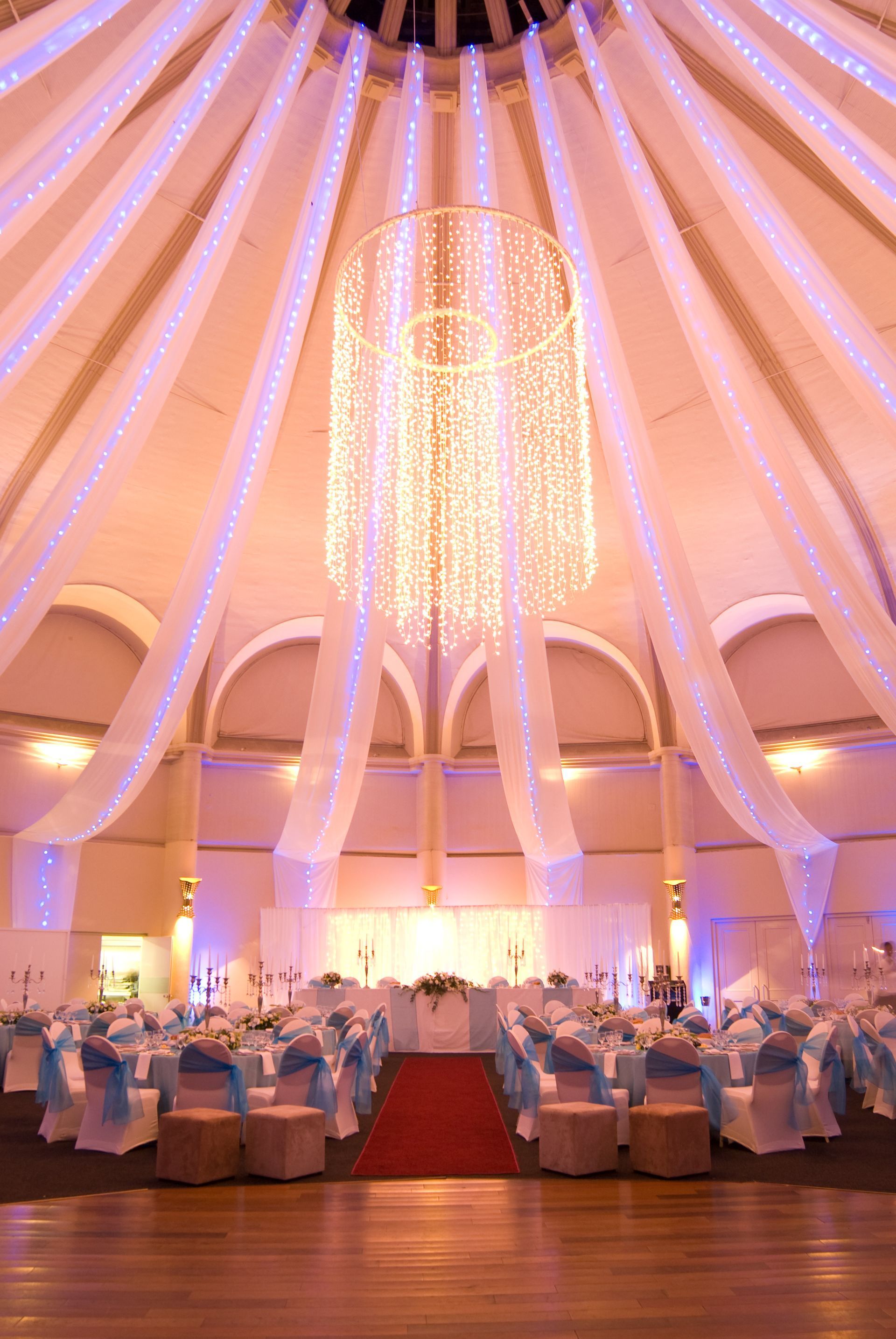 A large room with tables and chairs set up for a wedding reception with a chandelier hanging from the ceiling.
