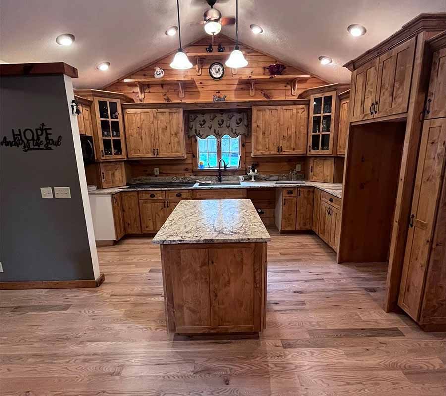 A rustic kitchen with wood cabinets, a granite-topped island, and a vaulted ceiling with hanging pendant lights.