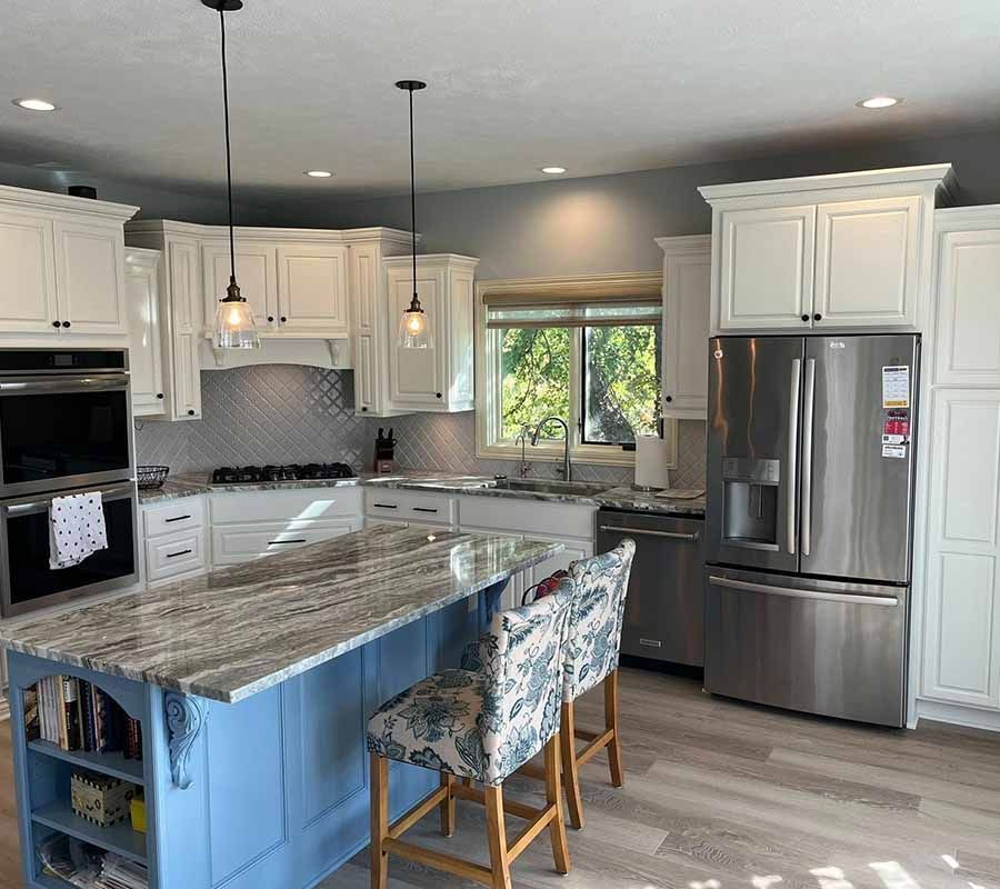 Modern kitchen with a light blue island, white cabinets, stainless steel appliances, and two floral bar stools.