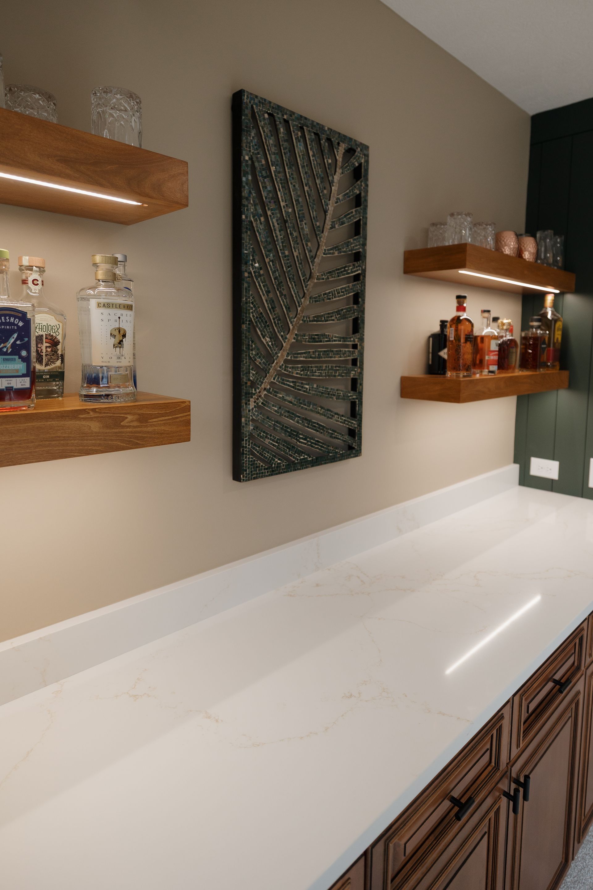A laundry room with sage green cabinets, light wood counters and flooring, a white subway tile backsplash, and a wood door.
