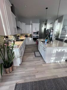 A bright, modern kitchen featuring white cabinets, a central island with hanging pendant lights, and light wood flooring.