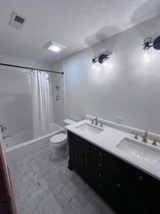 A bathroom with a black double vanity, white marble-style flooring, and a white shower-tub combination.