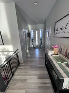 A brightly lit residential hallway with light wood flooring, a black console table on the right, and a metal railing.