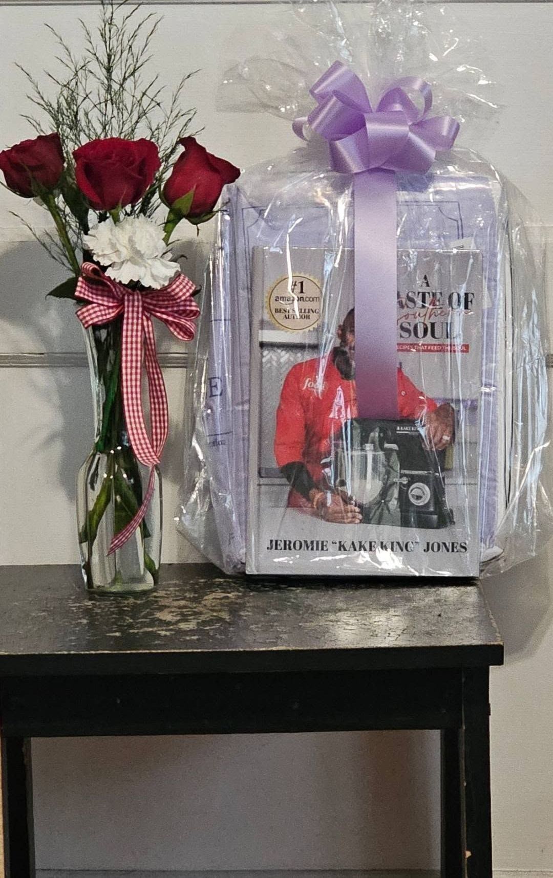 A picture of a man in a red shirt is wrapped in plastic and sitting on a table next to a vase of flowers.