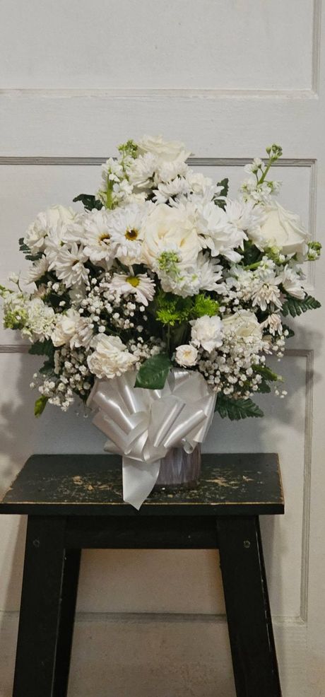 A vase filled with white flowers is sitting on a black stool.