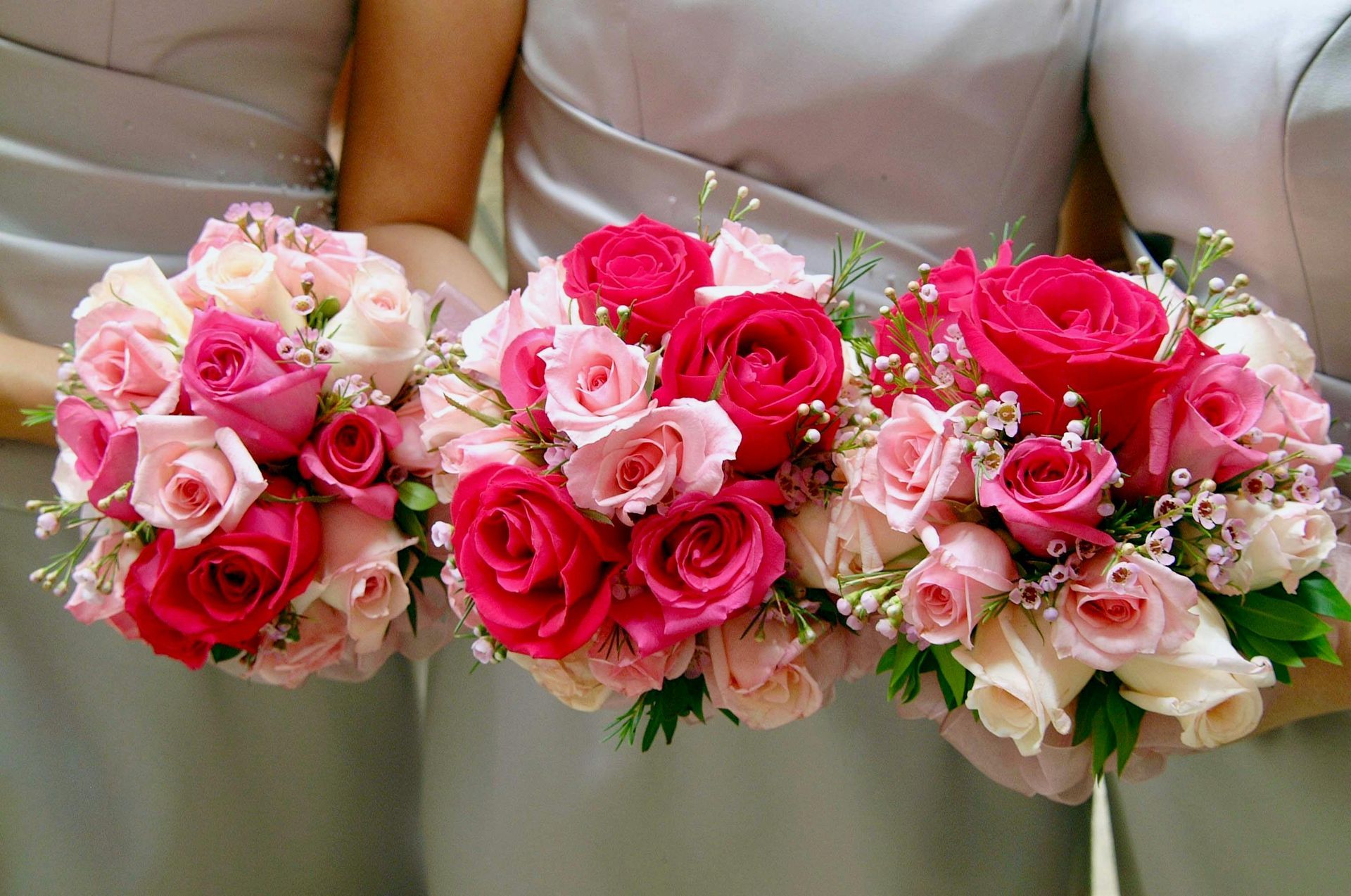 Three bridesmaids are holding bouquets of pink roses