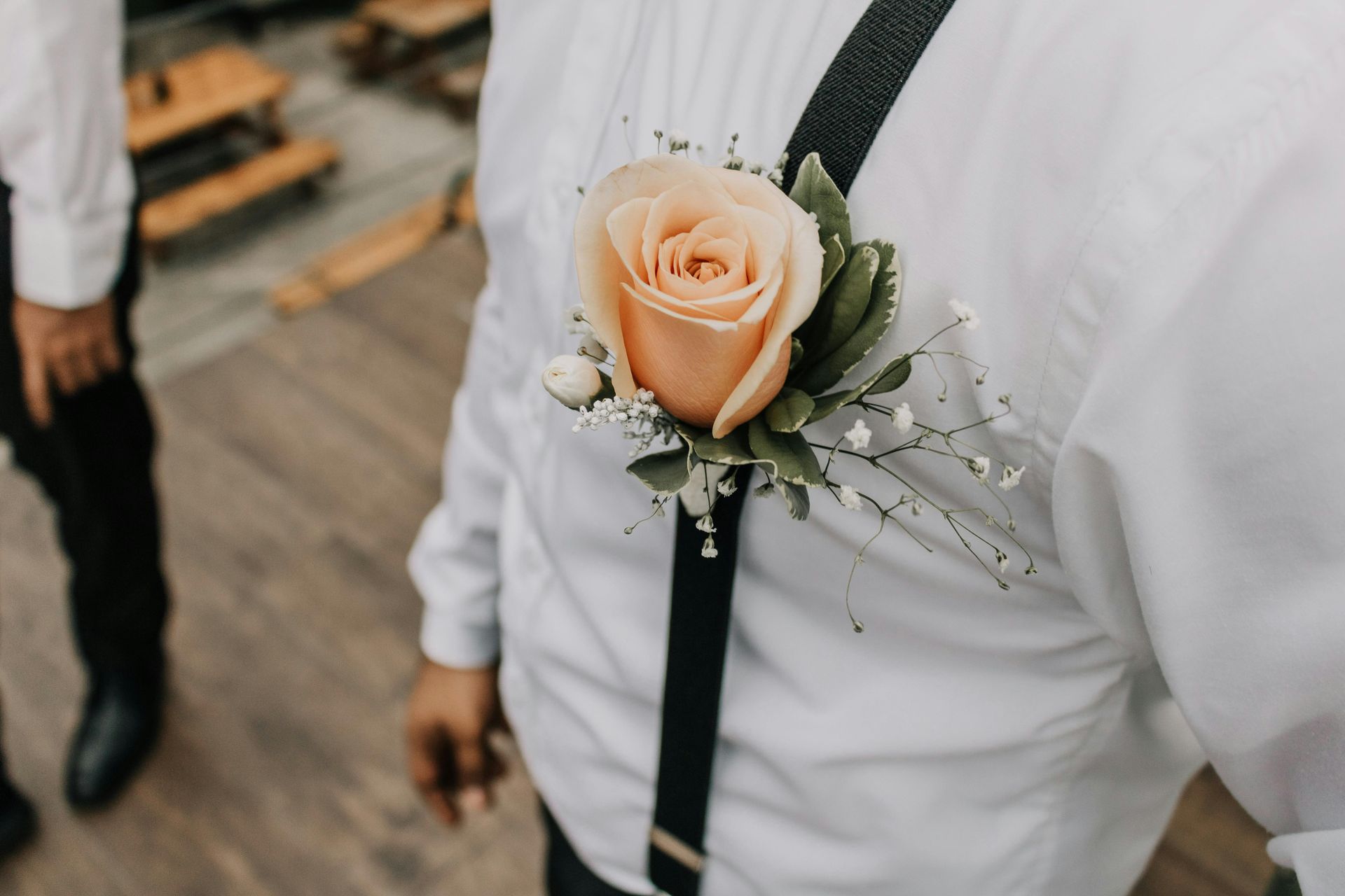 A man wearing suspenders and a buttonhole with a rose on his chest.