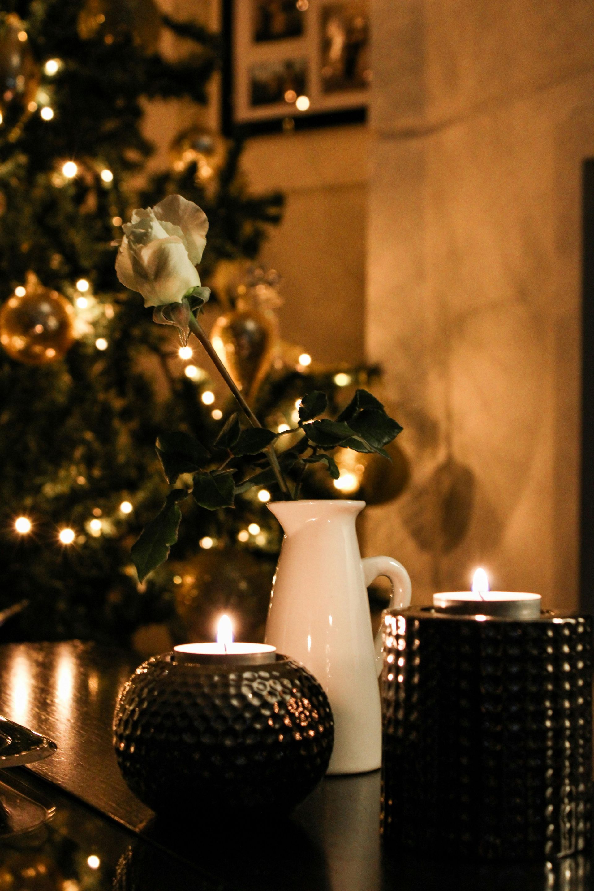 A christmas tree is behind a table with candles and a vase of flowers.