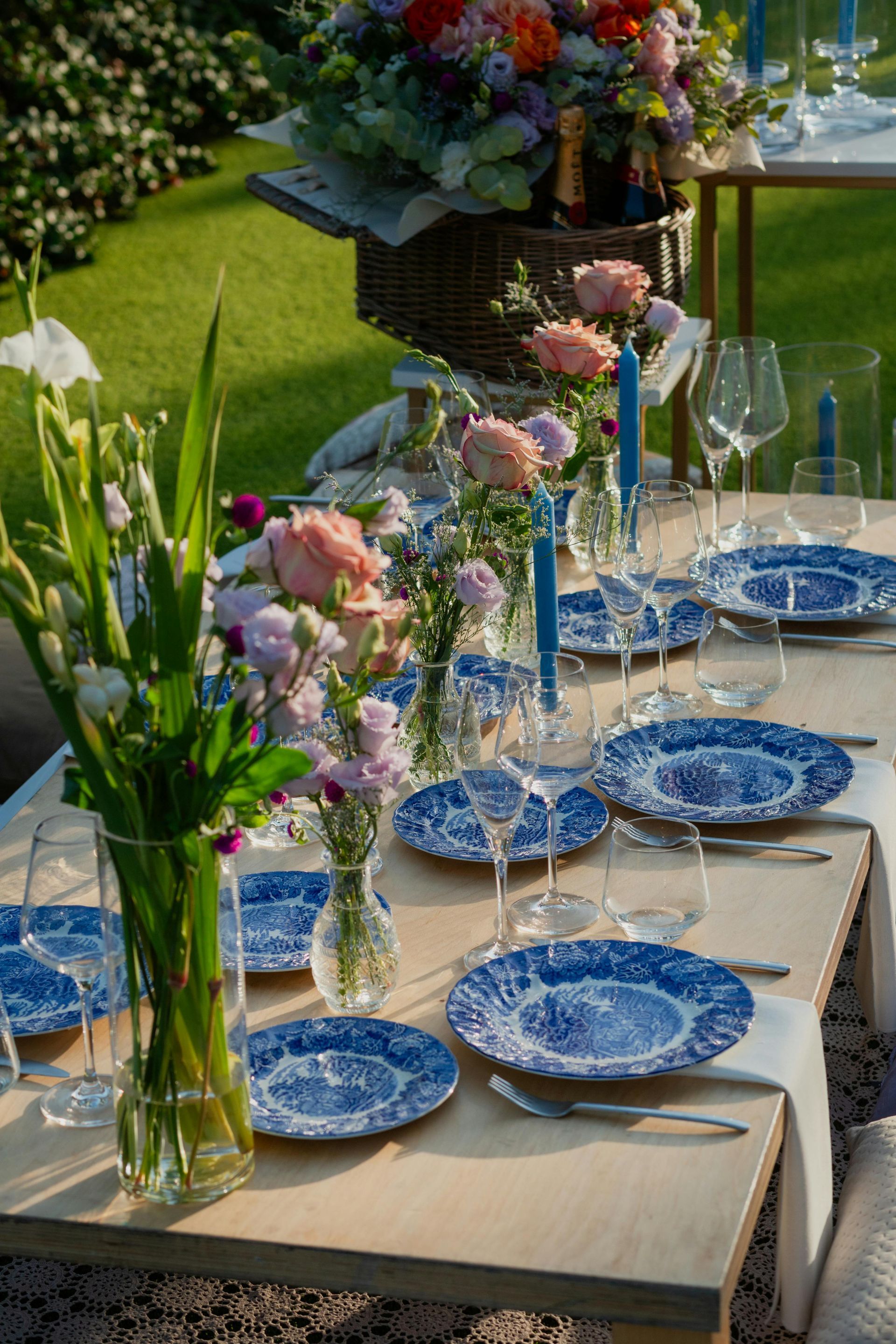 A table set with blue and white plates , candles , and vases of flowers.