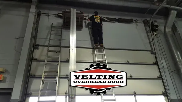 A man on a ladder working on a overhead door for velting overhead door