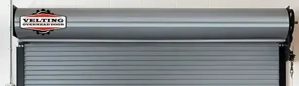 A gray rolling garage door is sitting on a white wall.