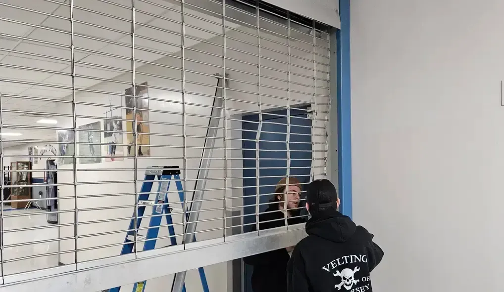 A man is standing in front of a window with a ladder in the background.