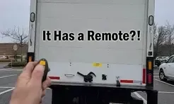 A person is holding a remote control in front of a white truck.