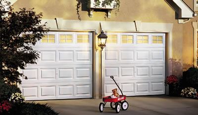 A red wagon with a teddy bear in it is parked in front of a garage door.