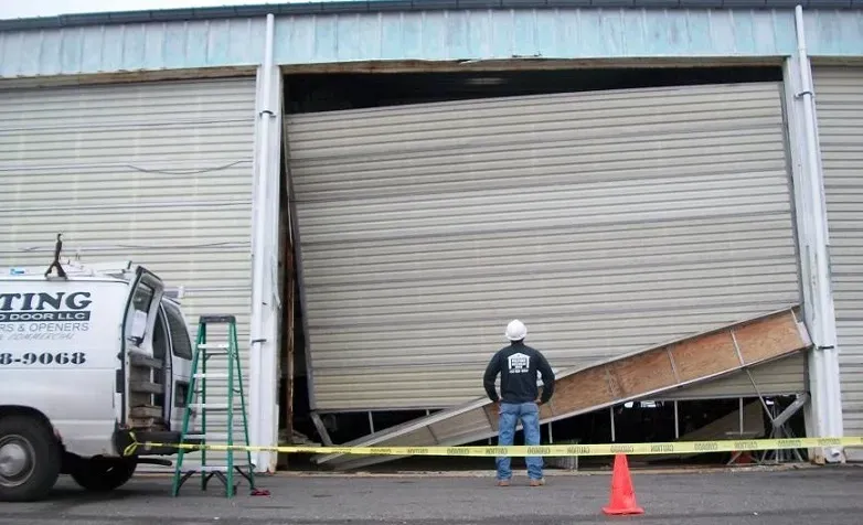 A man is standing in front of a damaged garage door.