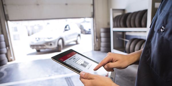 A man is using a tablet in a garage with a car in the background.