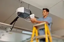 A man is standing on a ladder fixing a garage door opener.