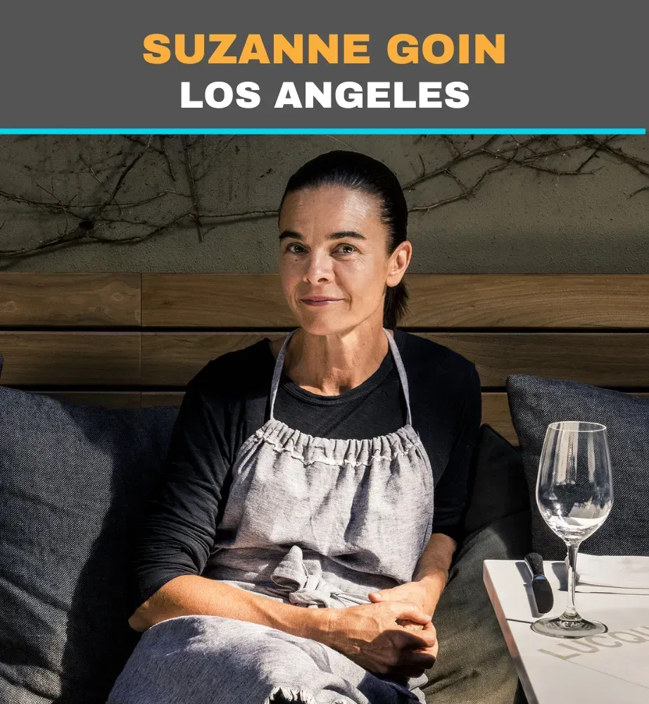 Suzanne Goin seated at a restaurant table in Los Angeles, wearing an apron and smiling at the camera