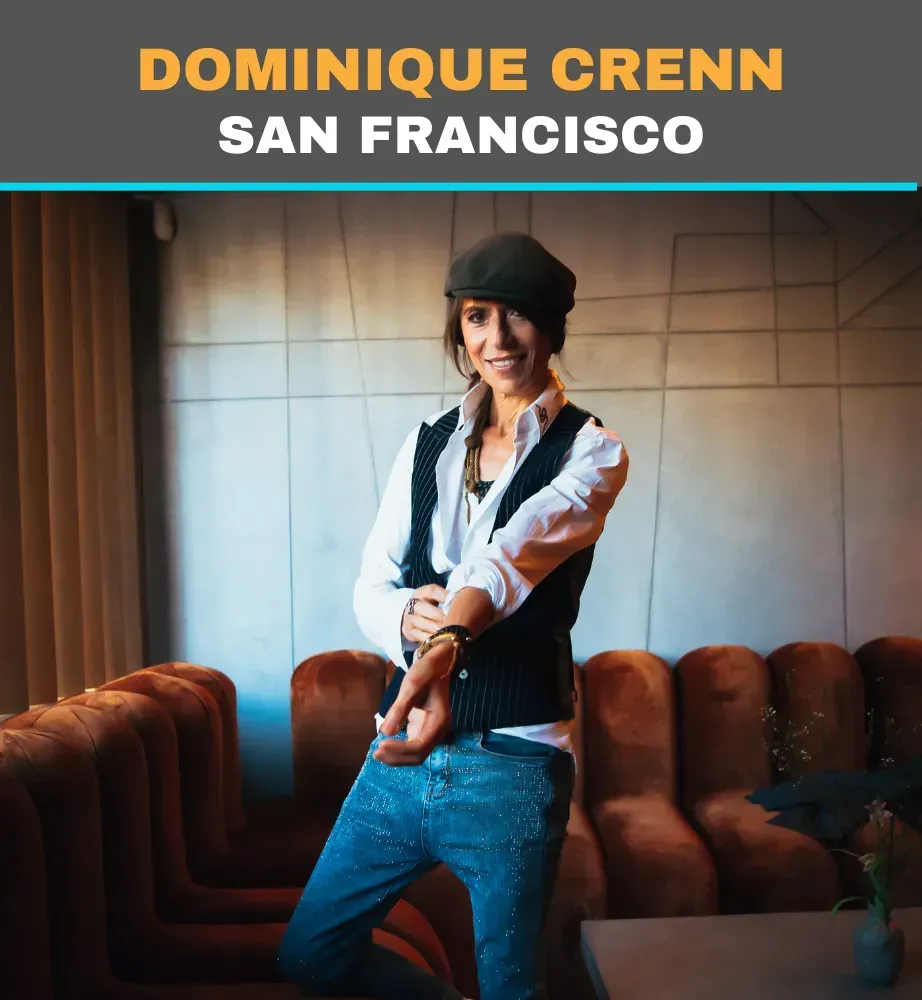 Dominique Crenn in a restaurant booth, smiling with crossed arms, under a “San Francisco” sign.
