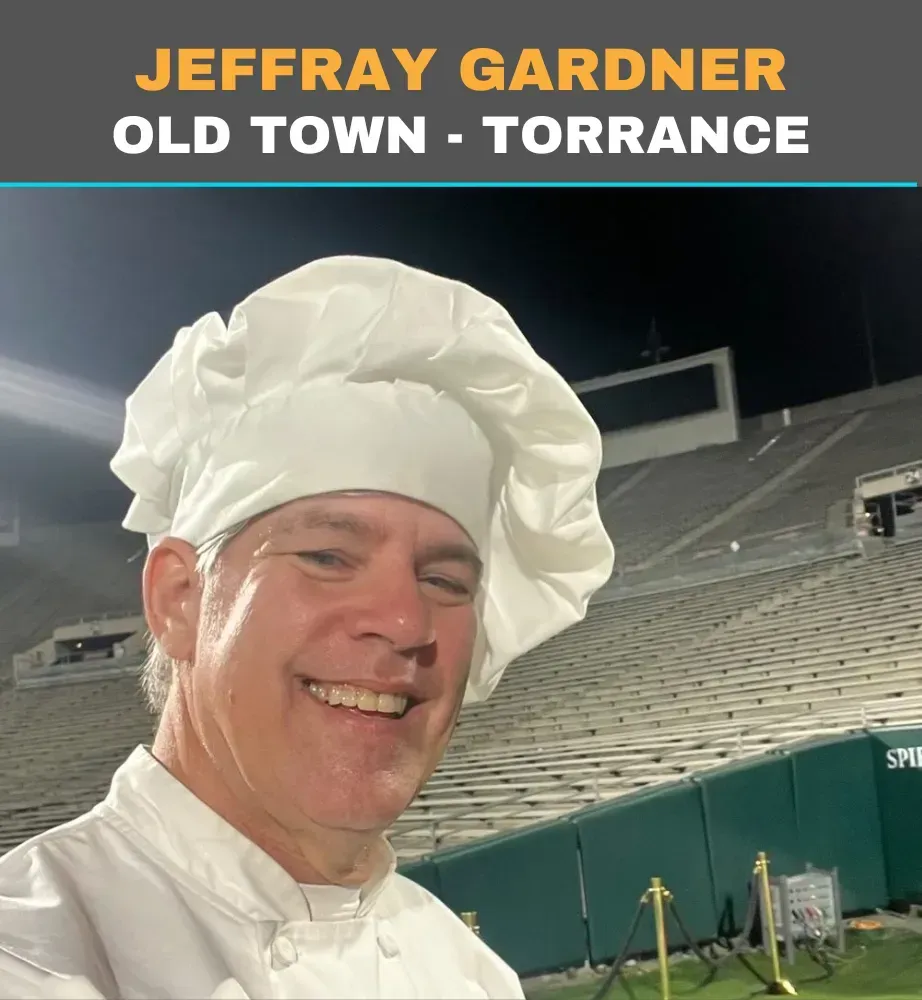 Jeffray Gardner smiling in a white chef hat at Old Town Torrance stadium at night