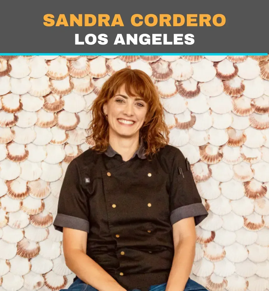 Sandra Cordero smiling in a black chef coat, standing before a white scalloped wall, labeled Los Angeles