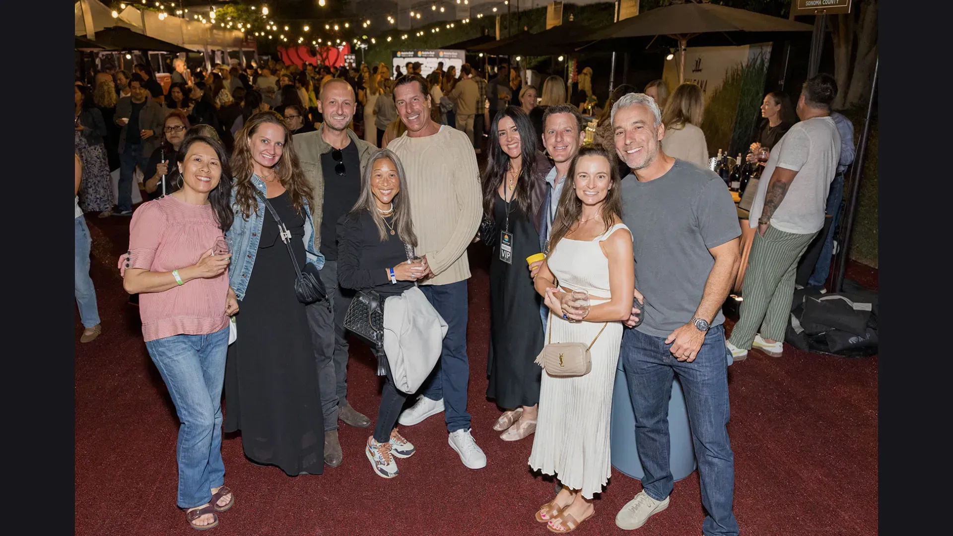 Group of people posing together at a nighttime event with string lights and a red carpet.