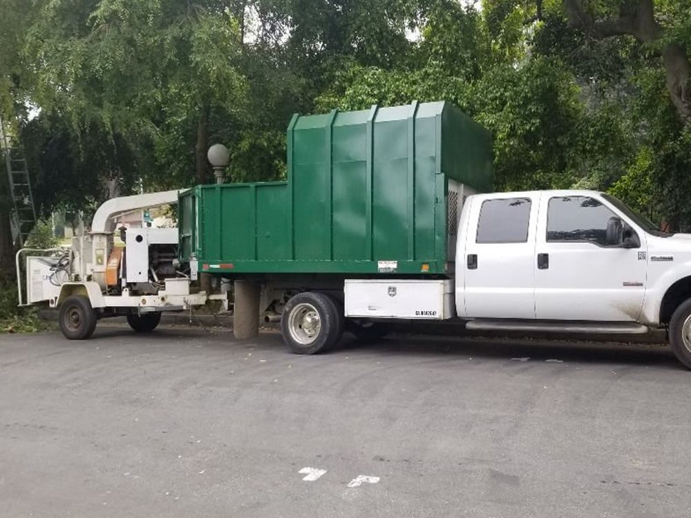 A white truck with a green trailer attached to it is parked next to a tree chipper.