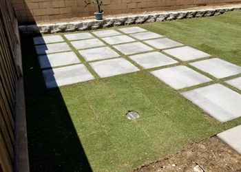 A concrete walkway leading to a lush green lawn.