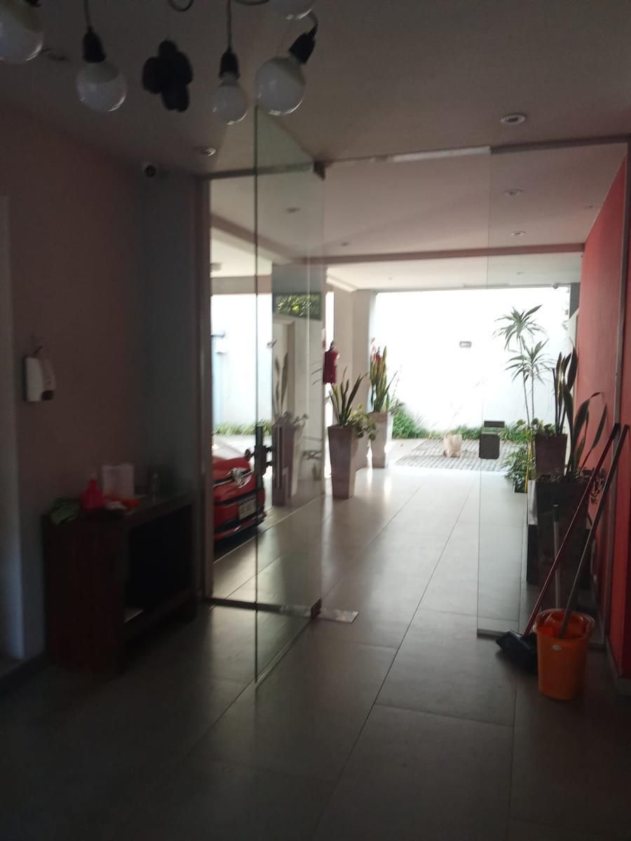 Pasillo de apartamento moderno con suelo de baldosas, pared con espejo, plantas en macetas y luz brillante en el balcón.