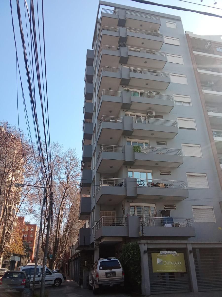 Edificio de apartamentos alto en una calle estrecha con árboles desnudos, coches aparcados