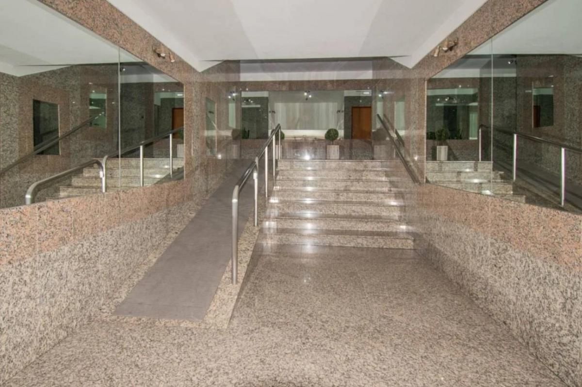 Vestíbulo del edificio con escalera central de mármol y barandillas de cristal, visto desde la entrada.