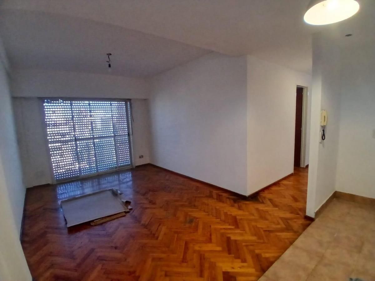 Habitación vacía con suelo de parqué, paredes blancas, una ventana y una lámpara de techo.