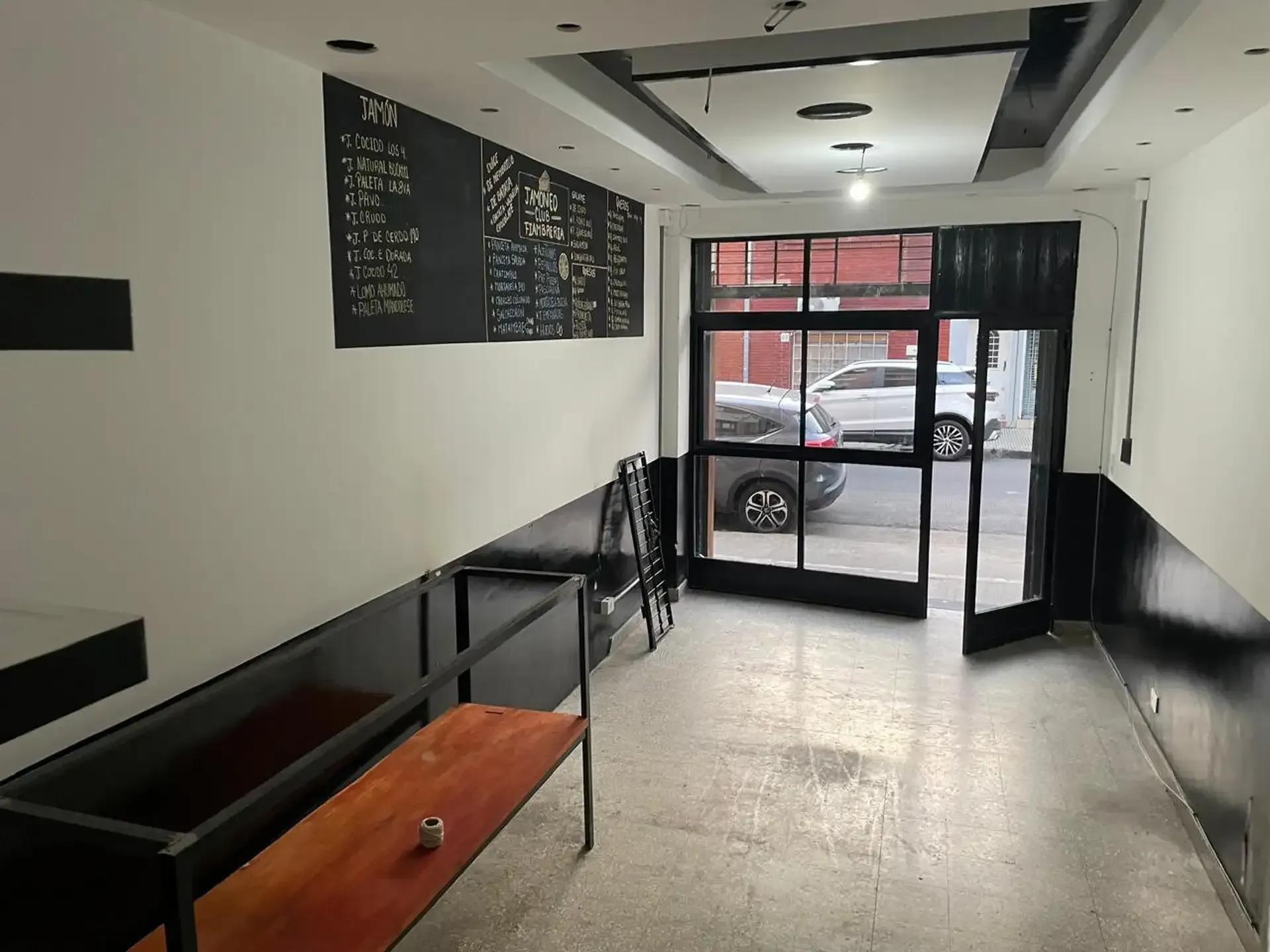 Pasillo de oficina moderno con entrada de cristal, paredes blancas y negras y un banco junto a la ventana.