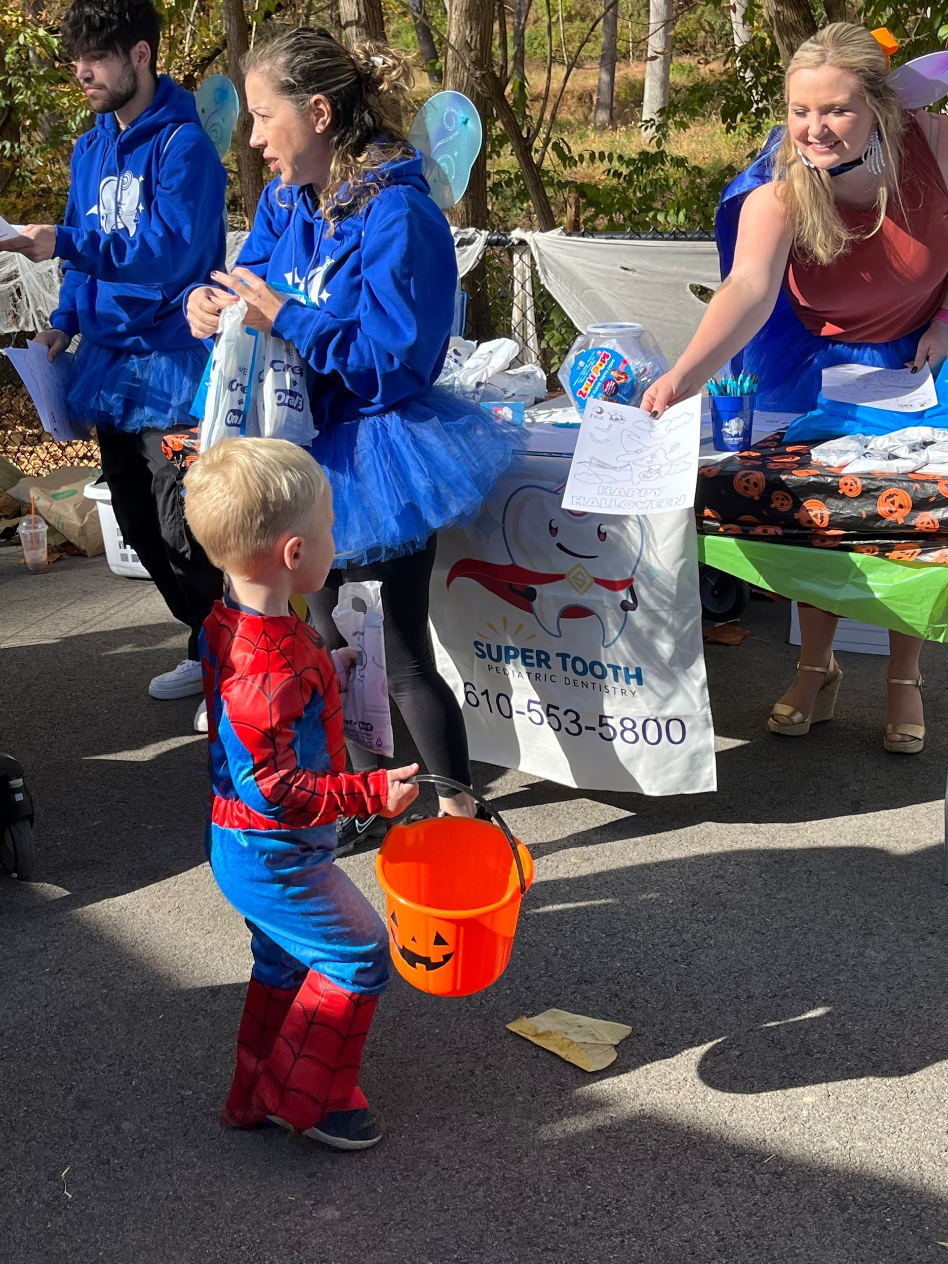 A little boy in a spiderman costume is holding a trick or treat bucket.