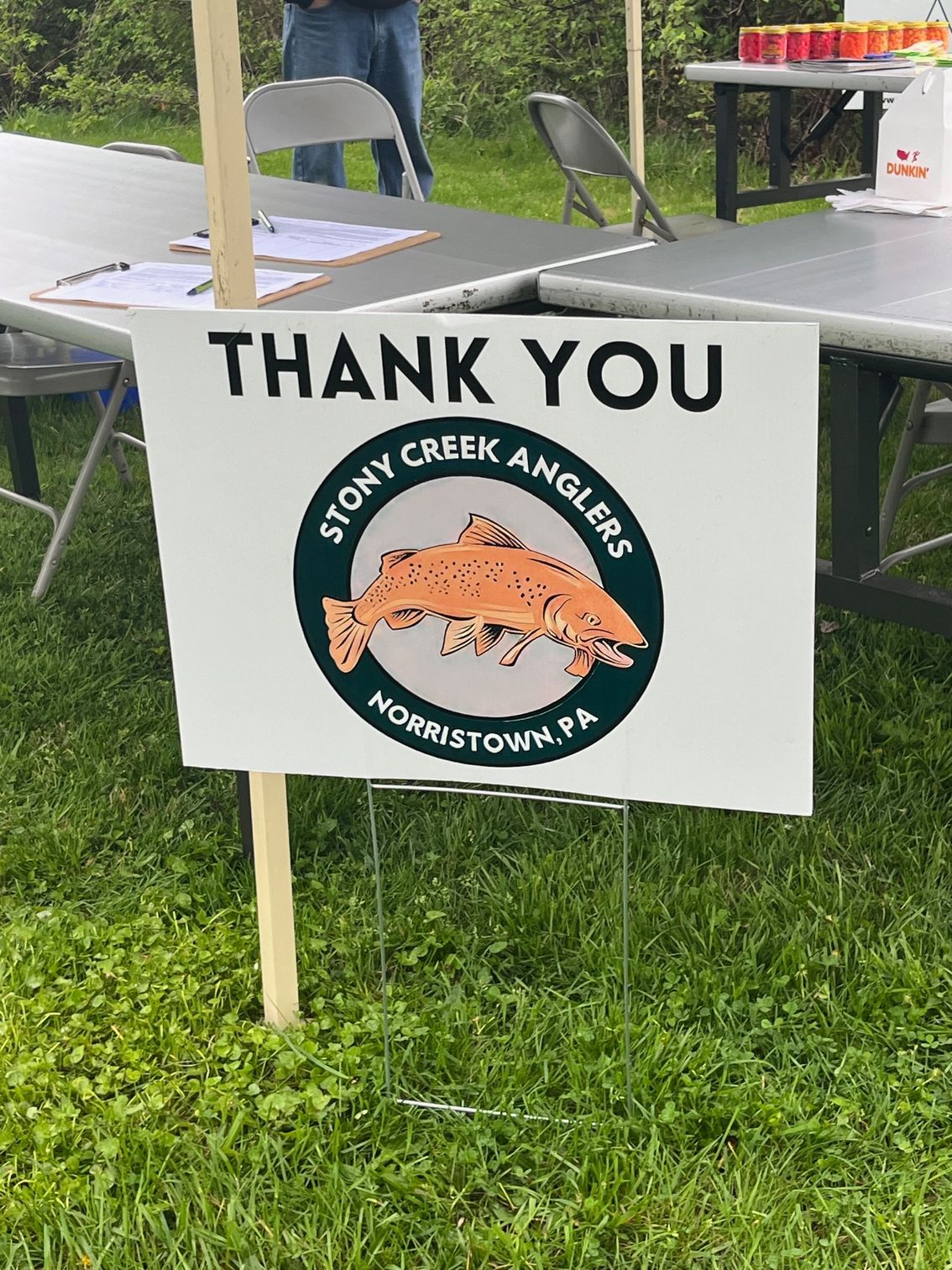 A thank you sign is sitting in the grass next to a table.