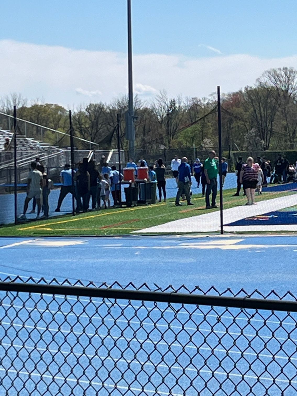 A group of people are standing on a tennis court behind a chain link fence.