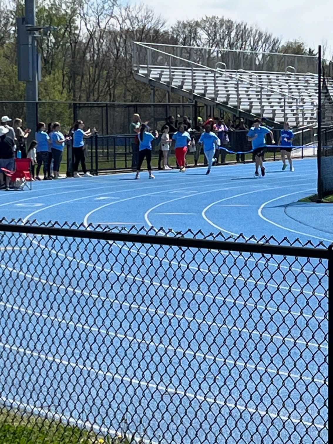 A group of people are running on a track behind a chain link fence