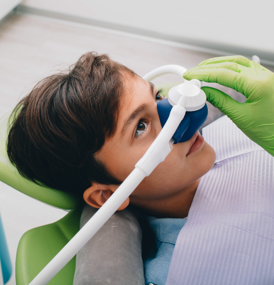 A young boy is laying in a dental chair with an oxygen mask on his face