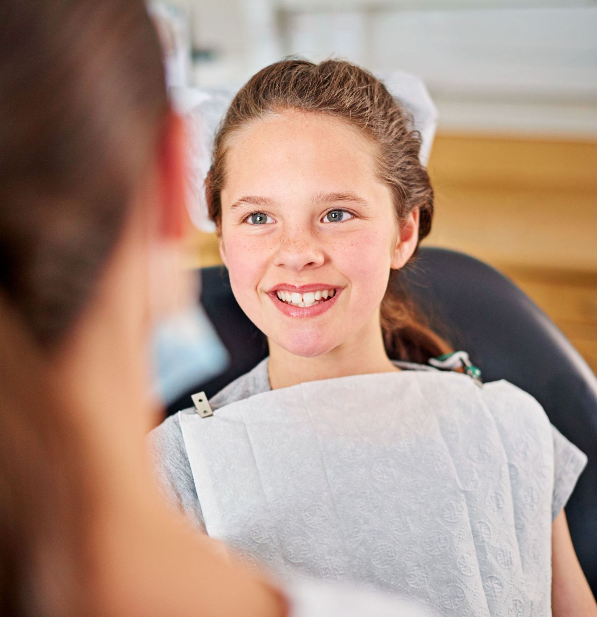 A young girl is smiling while sitting in a dental chair.