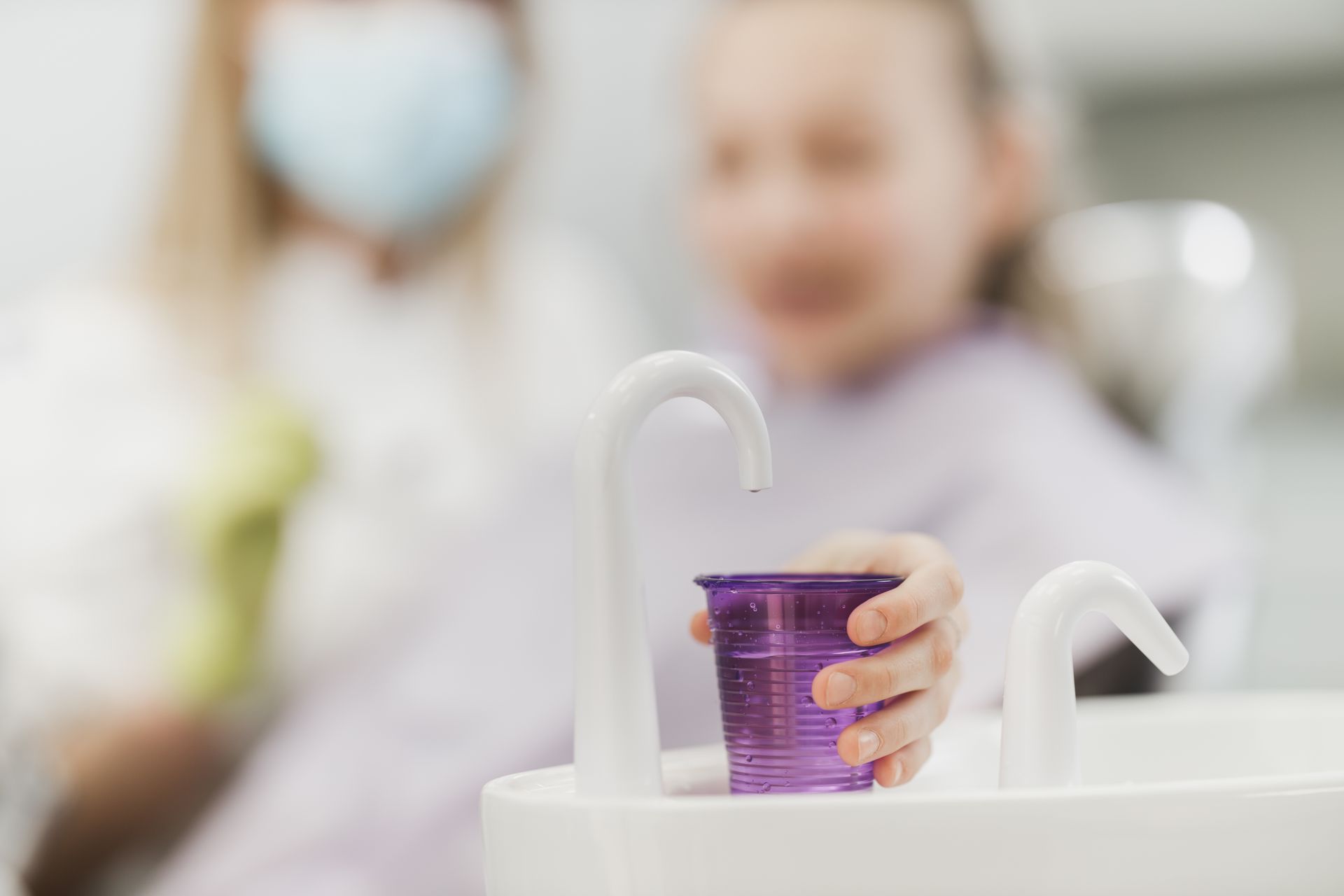 A young girl is sitting in a dental chair holding a cup of mouthwash.