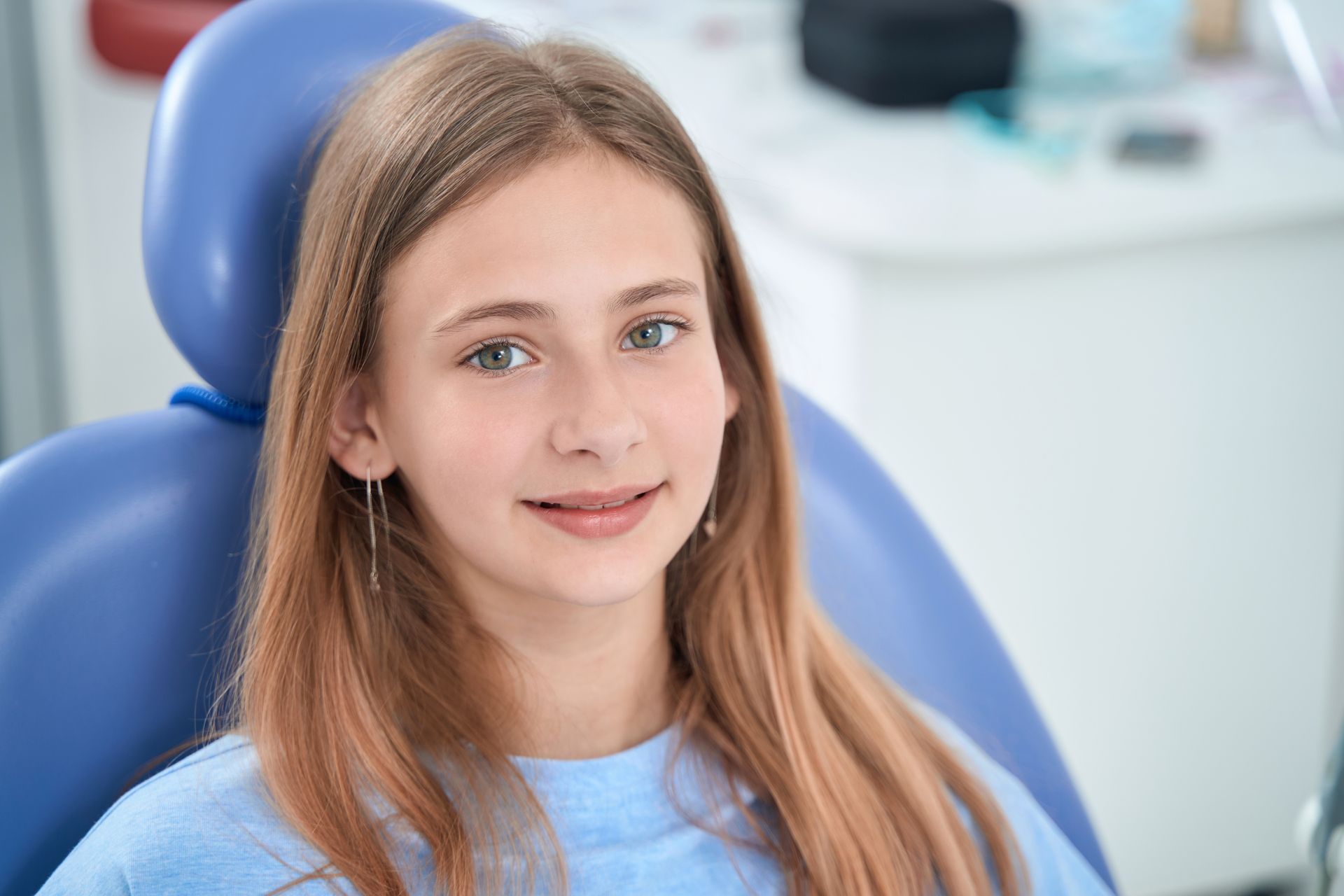 A young girl is sitting in a dental chair and smiling at the camera.