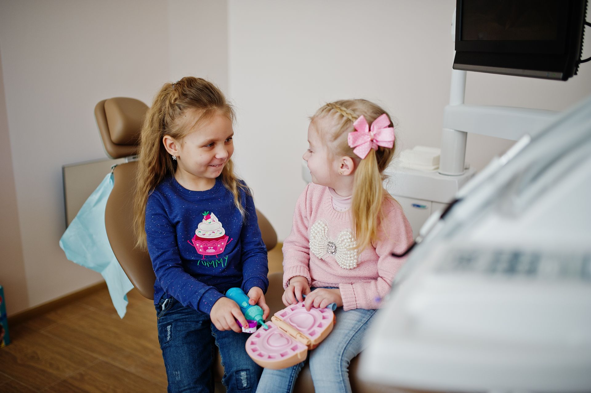 Two little girls are sitting in a dental chair playing with toys.