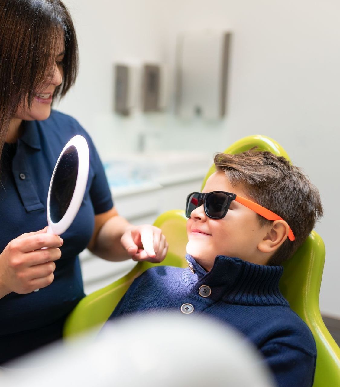 A woman is looking at a young boy 's teeth in a mirror.