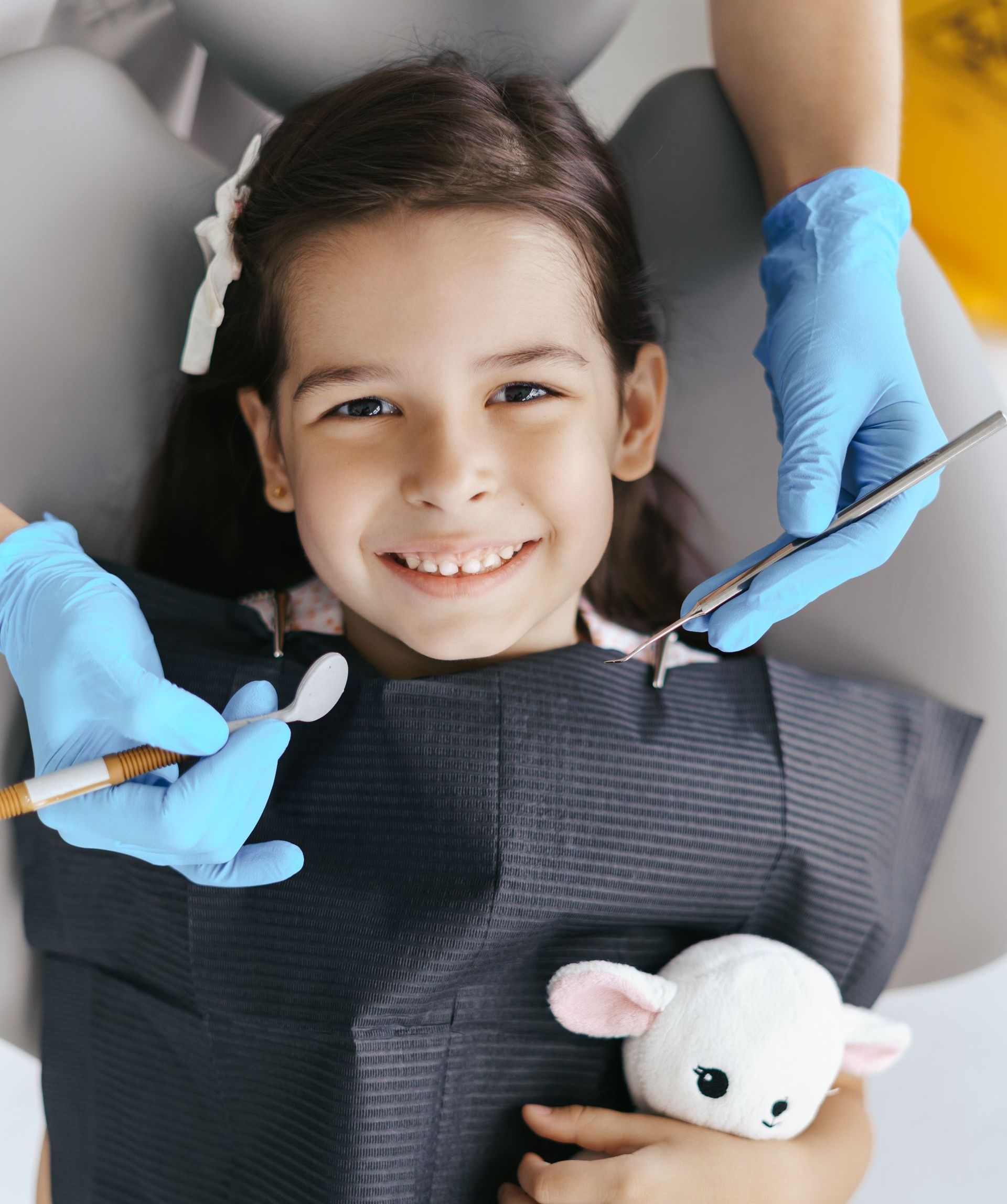 A little girl is getting her teeth examined by a dentist while holding a stuffed animal.